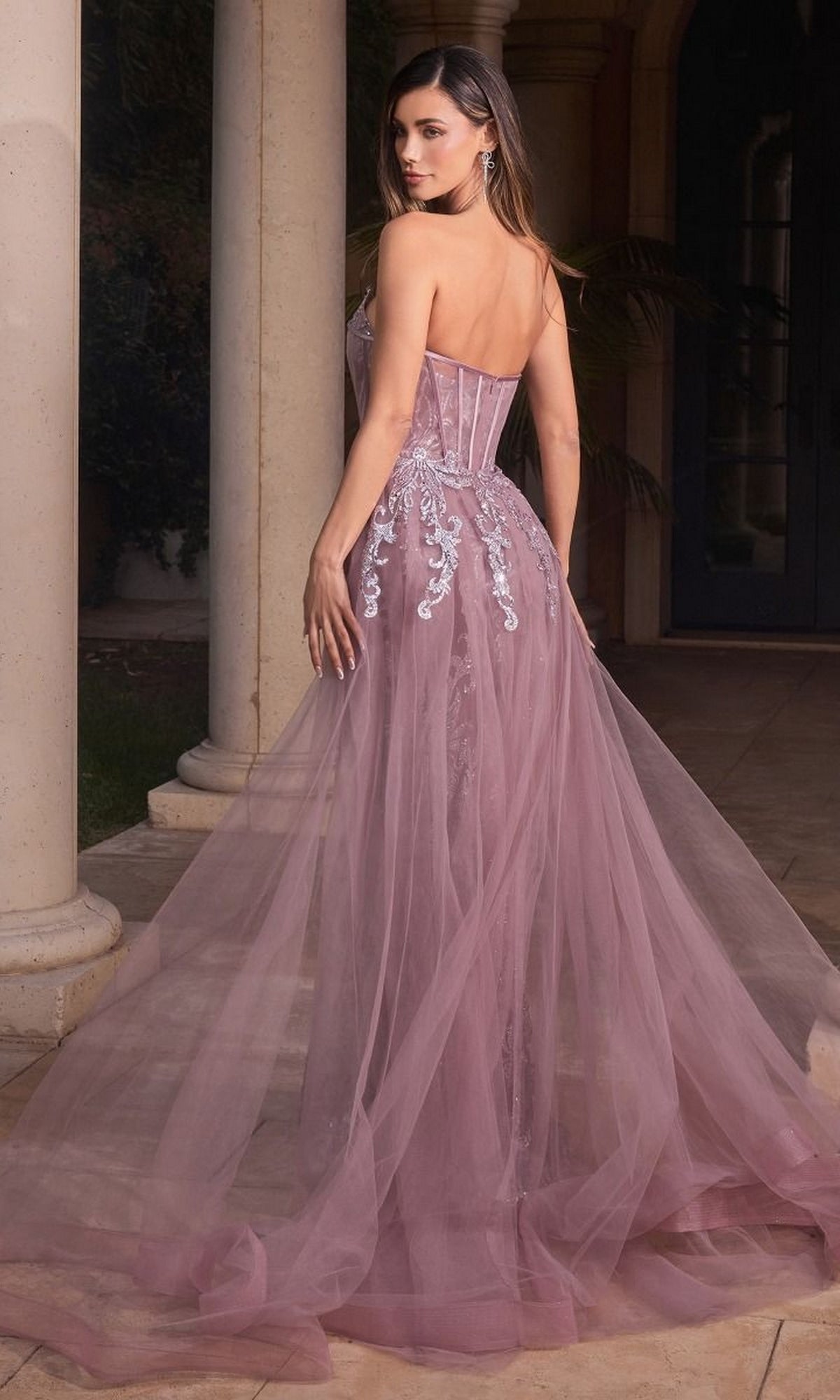 A woman wearing the Glitter-Print Strapless Long Prom Dress J858 with sheer lavender fabric and embroidered details stands outdoors, facing away and looking over her shoulder.